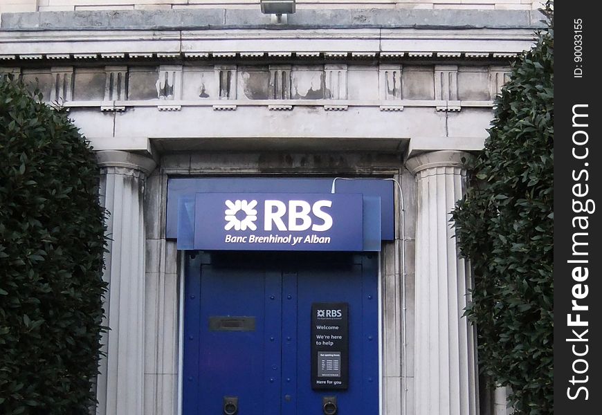 A Welsh version of the RBS name for a Welsh branch in 2011. Destined to be a thing of the past, as the English and Welsh branches of RBS are due for sell-off. For the uninitiated, the government support package that stopped RBS collapsing in 2009 resulted in a requirement that the 300-odd branches of RBS in England and Wales be sold off. The plan has changed many times. A planned sell-off to Santander collapsed. Then RBS decided to create and float a new standalone bank using these branches, the NatWest branches in Scotland and the long-dormant Williams and Glyn brand they owned. By summer 2016, questions about the financial viability of the proposed new business and the difficulty of creating a new IT infrastructure saw the plan shelved. Branches like this one are now back on the market - and may yet end up with Santander, five years later on!. A Welsh version of the RBS name for a Welsh branch in 2011. Destined to be a thing of the past, as the English and Welsh branches of RBS are due for sell-off. For the uninitiated, the government support package that stopped RBS collapsing in 2009 resulted in a requirement that the 300-odd branches of RBS in England and Wales be sold off. The plan has changed many times. A planned sell-off to Santander collapsed. Then RBS decided to create and float a new standalone bank using these branches, the NatWest branches in Scotland and the long-dormant Williams and Glyn brand they owned. By summer 2016, questions about the financial viability of the proposed new business and the difficulty of creating a new IT infrastructure saw the plan shelved. Branches like this one are now back on the market - and may yet end up with Santander, five years later on!