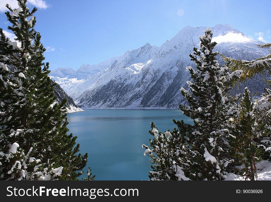 Scenic view of alpine lake and forest with snow capped mountains in background. Scenic view of alpine lake and forest with snow capped mountains in background.