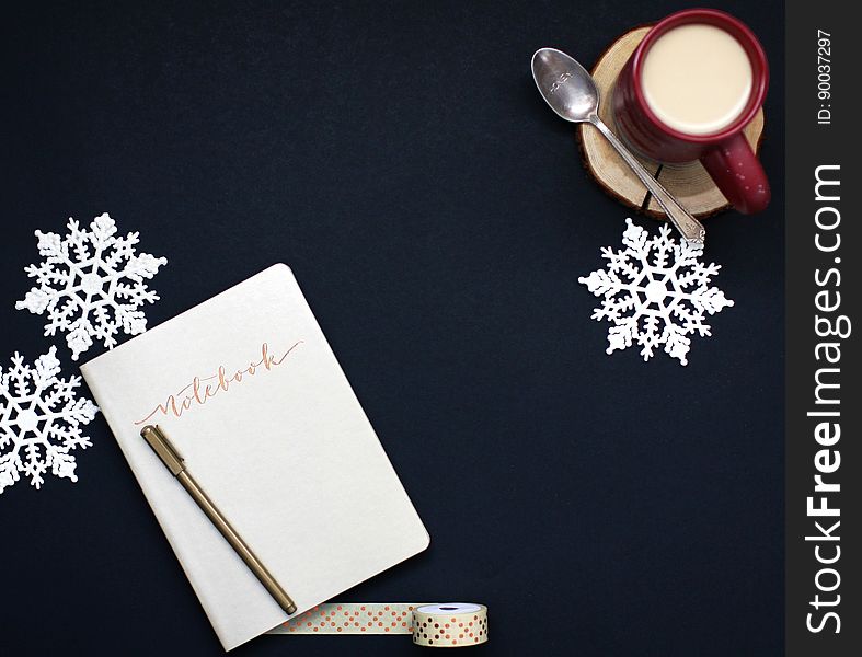 A notebook with a pen, a cup of coffee with milk, duct tape, and snowflake decorations. A notebook with a pen, a cup of coffee with milk, duct tape, and snowflake decorations.