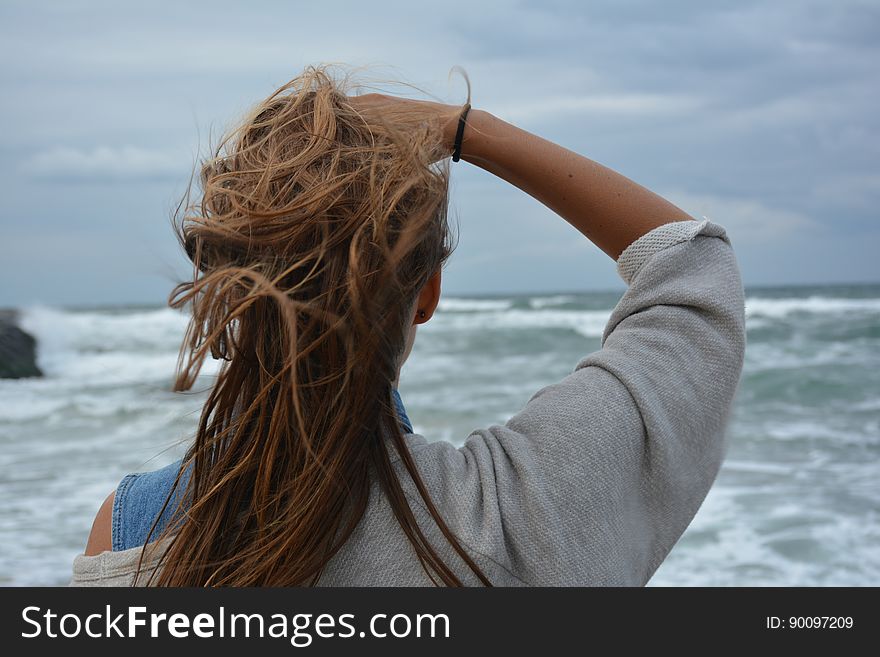 A woman standing by the sea with wind in her hair. A woman standing by the sea with wind in her hair.