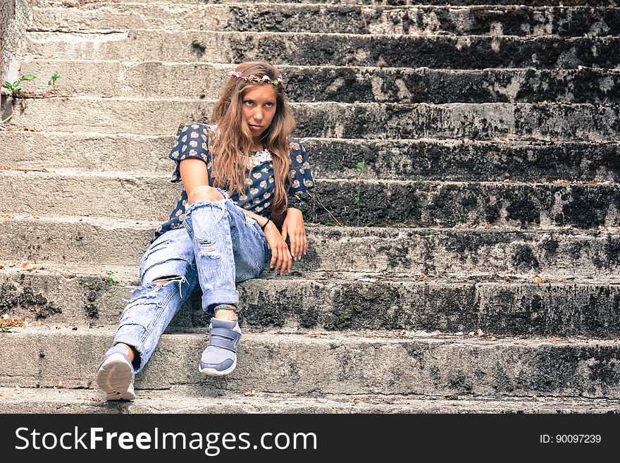 A woman wearing torn jeans and wreath of flowers sitting on concrete stairs. A woman wearing torn jeans and wreath of flowers sitting on concrete stairs.