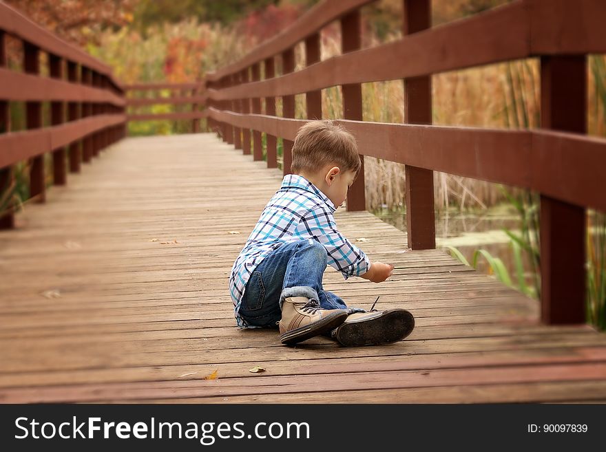 A young boy sitting on a pier by the lake. A young boy sitting on a pier by the lake.