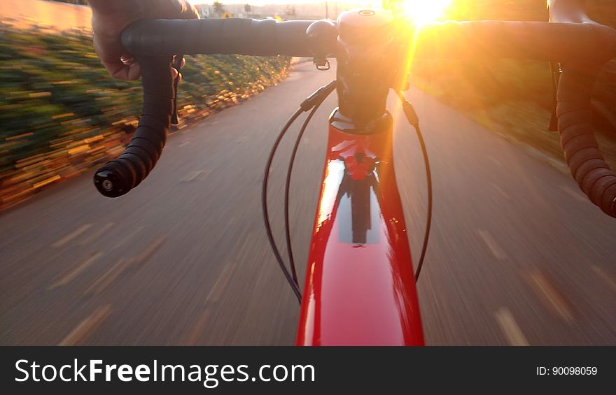 Hands of person riding racing bicycle on road with sun glistening off handlebars.