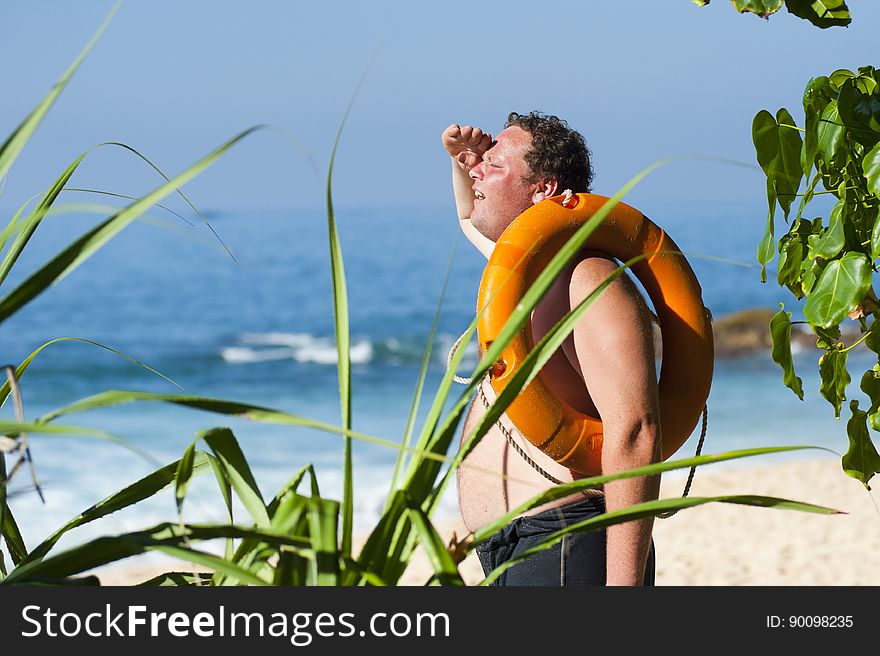 Man relaxing on tropical beach with inflatable ring over shoulder.