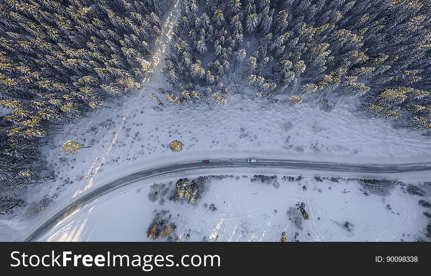 Aerial view of traffic on snowy road through forest on sunny day. Aerial view of traffic on snowy road through forest on sunny day.