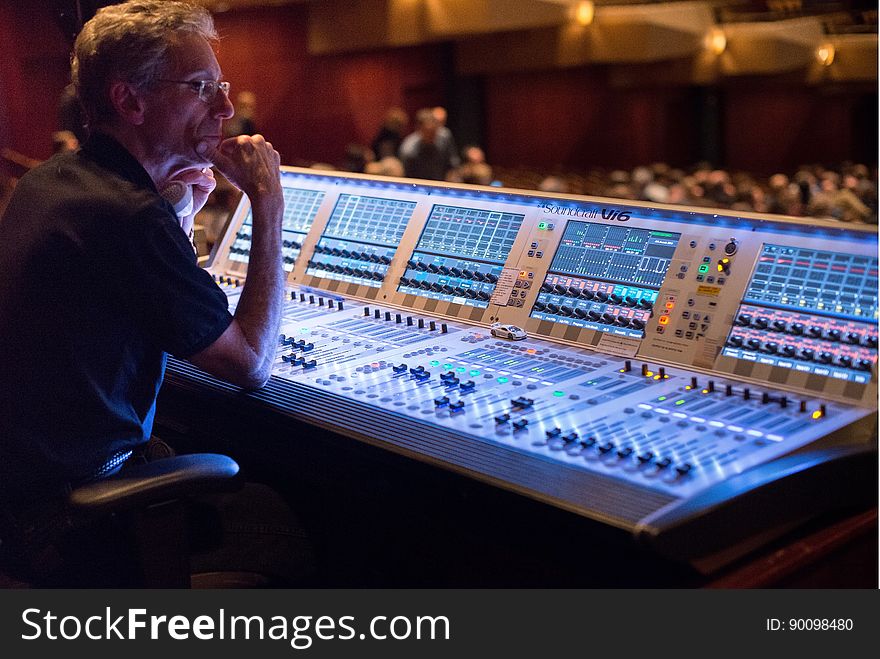 Man sitting at electronic sound mixing console inside theater. Man sitting at electronic sound mixing console inside theater.
