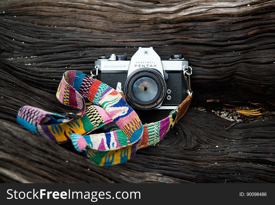 Pentax camera with colorful cloth strap on wooden log. Pentax camera with colorful cloth strap on wooden log.