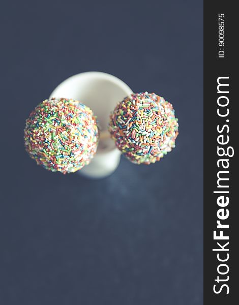 A pair of cake pops with colorful sprinkles.