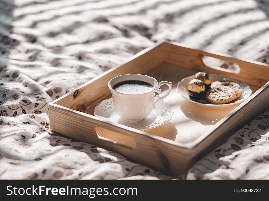 Wooden serving tray with white china cup and saucer filled with coffee and plate of cookies on tablecloth. Wooden serving tray with white china cup and saucer filled with coffee and plate of cookies on tablecloth.
