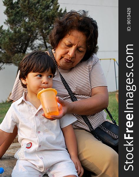 Grandmother feeding her grandson water from a sippy cup.