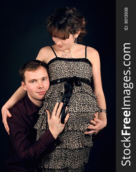 Young beautiful married couple the birth of the second child wait. Dark background. New photos every week