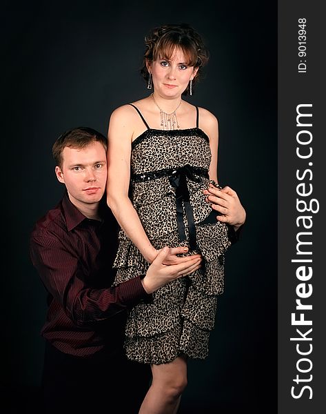 Young beautiful married couple the birth of the second child wait. Dark background. New photos every week