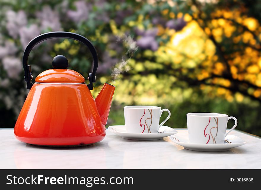 Orange teapot that contains smoking hot tea in front of a blurred background. Orange teapot that contains smoking hot tea in front of a blurred background