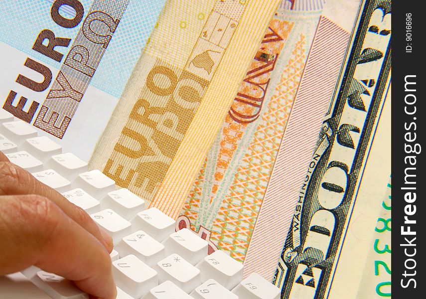 Fingers using computer keyboard overlaid over currency bank notes. Fingers using computer keyboard overlaid over currency bank notes