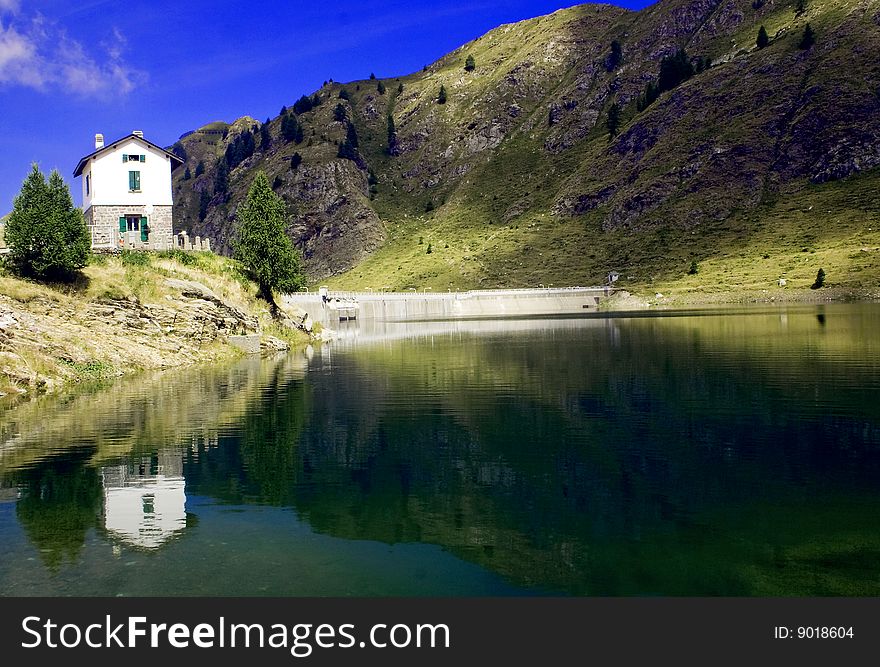 Artificial dam with mountains and sky blue house