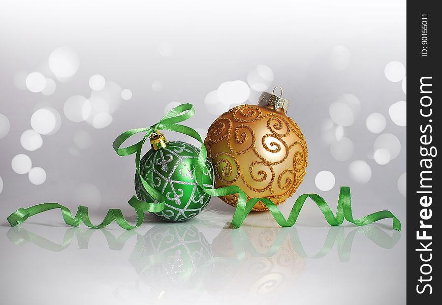 Green and gold Christmas tree ornament balls with green ribbon against white bokeh lights. Green and gold Christmas tree ornament balls with green ribbon against white bokeh lights.