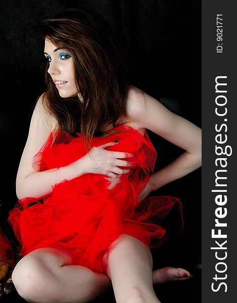 Female model covering her self in red nettiing. Sitting on a puffy against a black back drop. Female model covering her self in red nettiing. Sitting on a puffy against a black back drop.