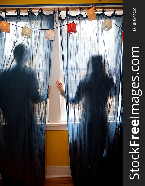 Young couple looking out a window behind blue curtains. Young couple looking out a window behind blue curtains.