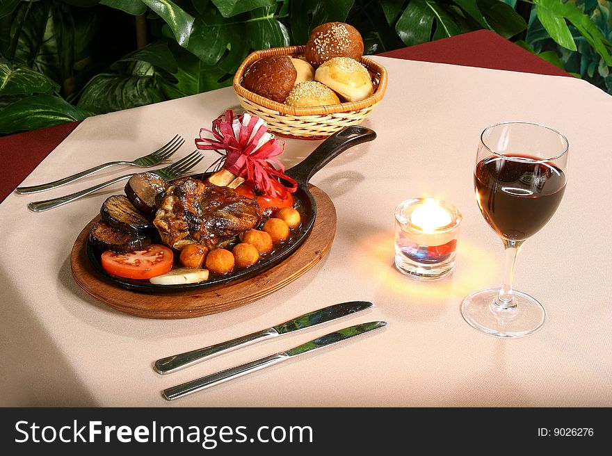 Fried meat on a table, wine, a candle and a roll
