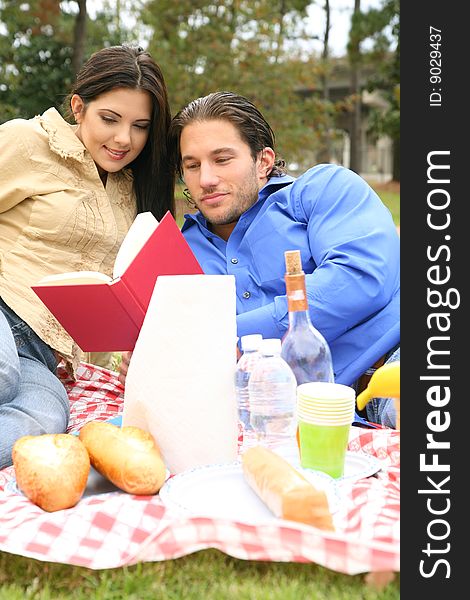 Young couple reading book together in outdoor picnic park. Young couple reading book together in outdoor picnic park