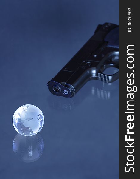 Glassy globe with pistol lying on dark background. Glassy globe with pistol lying on dark background