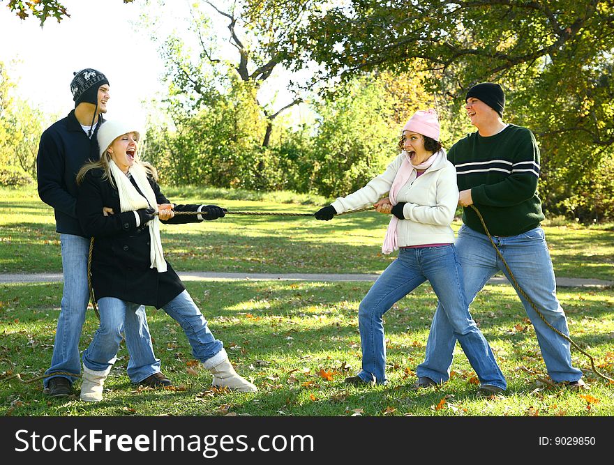 Four friends in playing tug of war in park