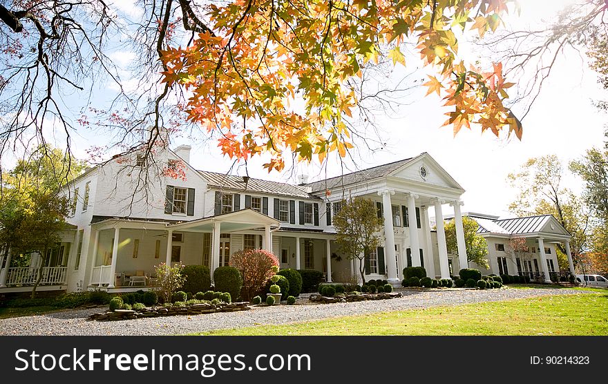 Exterior of white estate home with green lawn on sunny day. Exterior of white estate home with green lawn on sunny day.