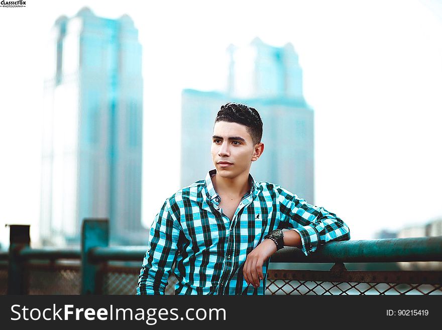 A young man leaning on a fence in the city.