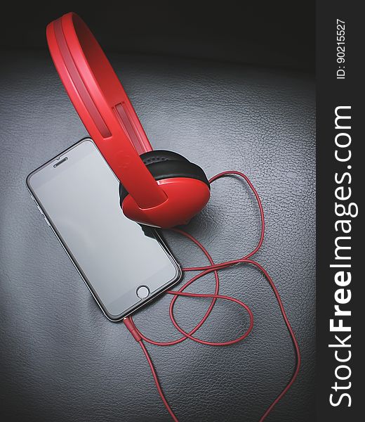 Red headphones attached to cell phone on grey leather. Red headphones attached to cell phone on grey leather.