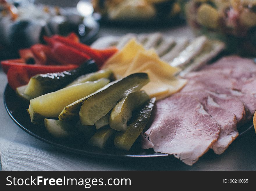 A plate of appetizers with pickles, meats, cheese and vegetables.