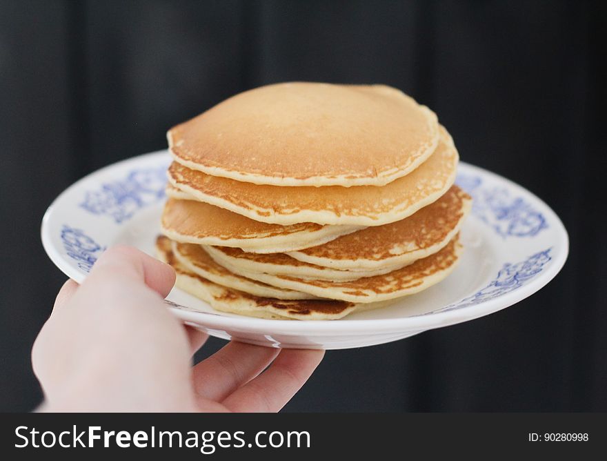 A person holding out a plate of thick American style pancakes. A person holding out a plate of thick American style pancakes.