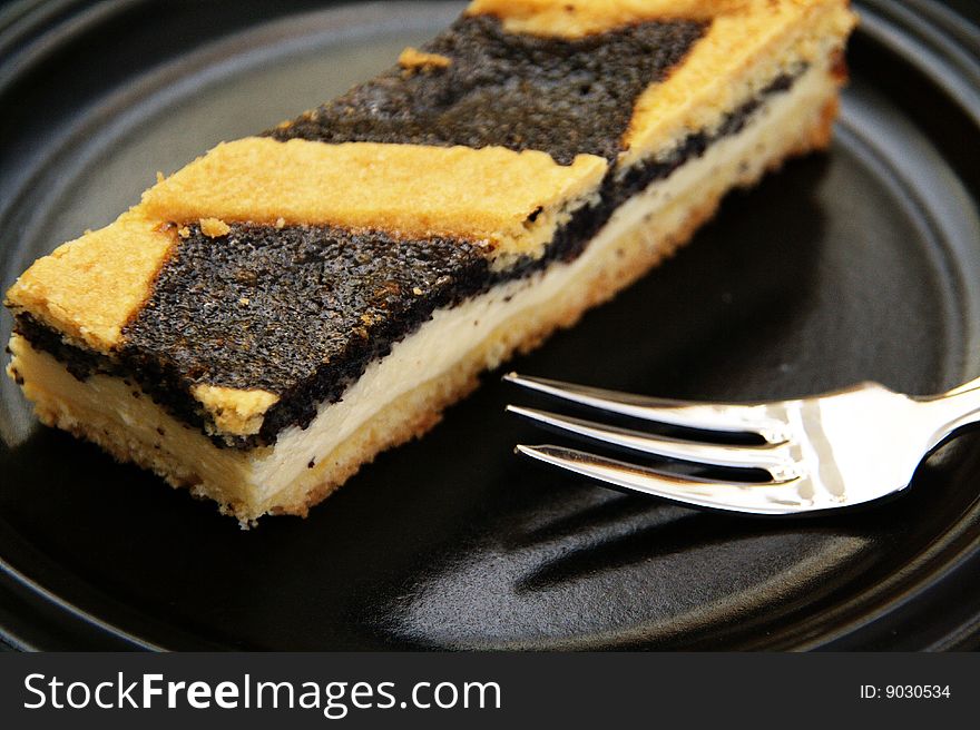 A piece of poppy-seed cake on a black plate with a fork beside it. A piece of poppy-seed cake on a black plate with a fork beside it.