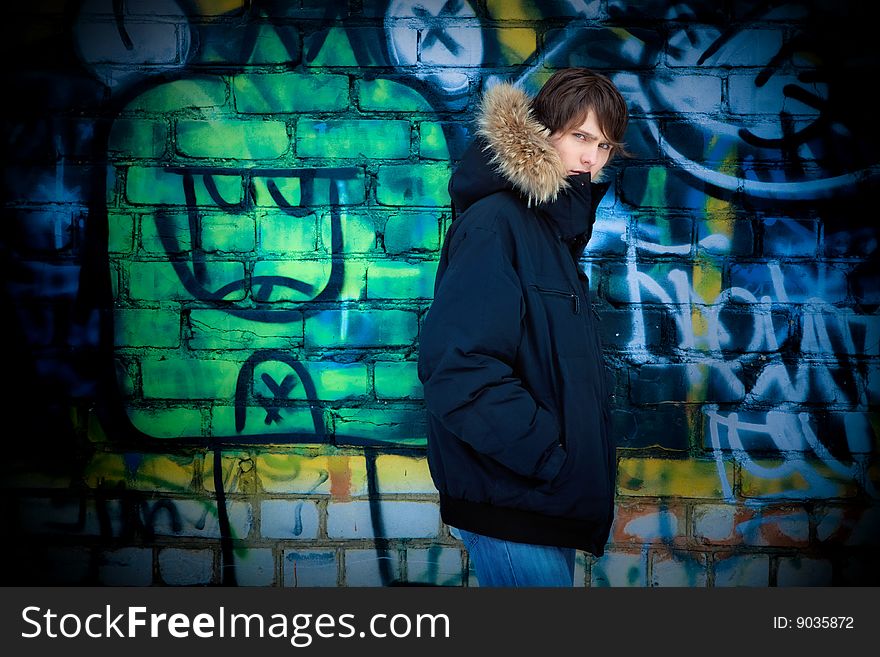 The young guy in a jacket with a hood costs near a wall. The young guy in a jacket with a hood costs near a wall