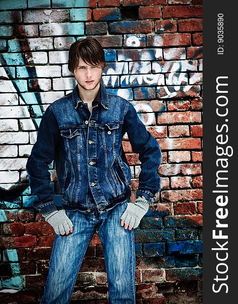 Young guy in jeans costs near to a brick wall. Young guy in jeans costs near to a brick wall