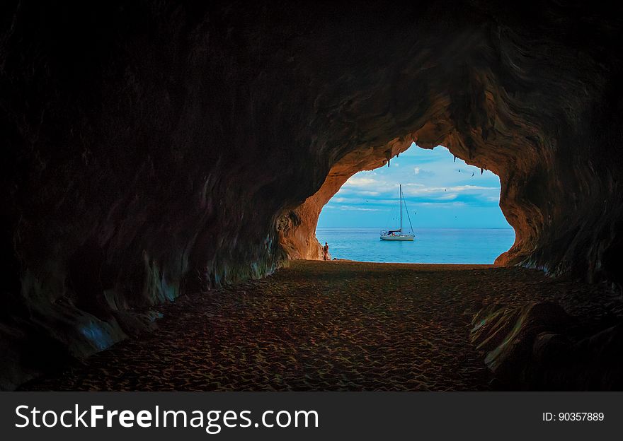 A view of a sailboat through an opening in a cave. A view of a sailboat through an opening in a cave.