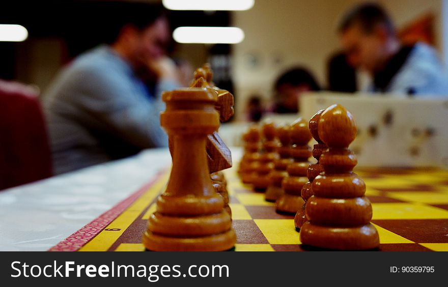 A close up of a chess board with chess players on the background.