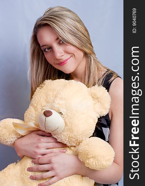 Young blonde girl sitting smiling with teddy-bear in front. Young blonde girl sitting smiling with teddy-bear in front