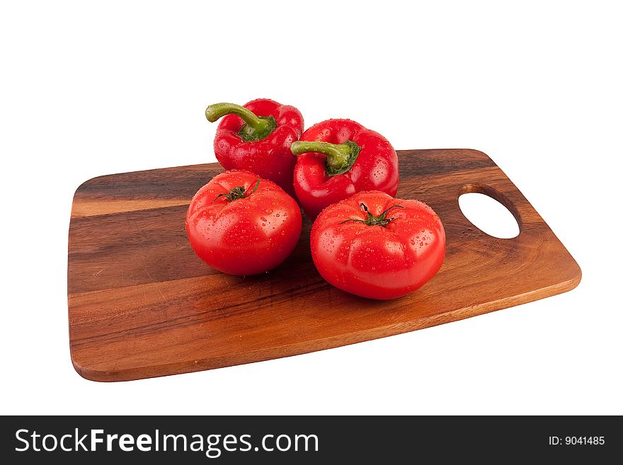 Two red peppers and two red tomatoes on cutting board. Isolated on white. Two red peppers and two red tomatoes on cutting board. Isolated on white.