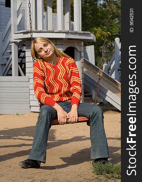 Girl in red pullover sitting on swing