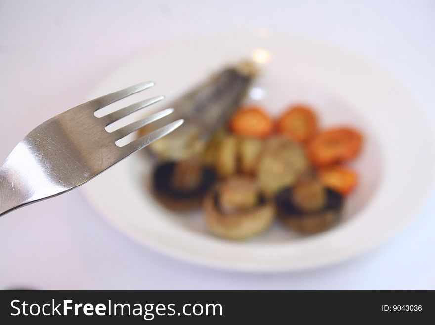 A fork in focus approaching an out of focus  plate with food