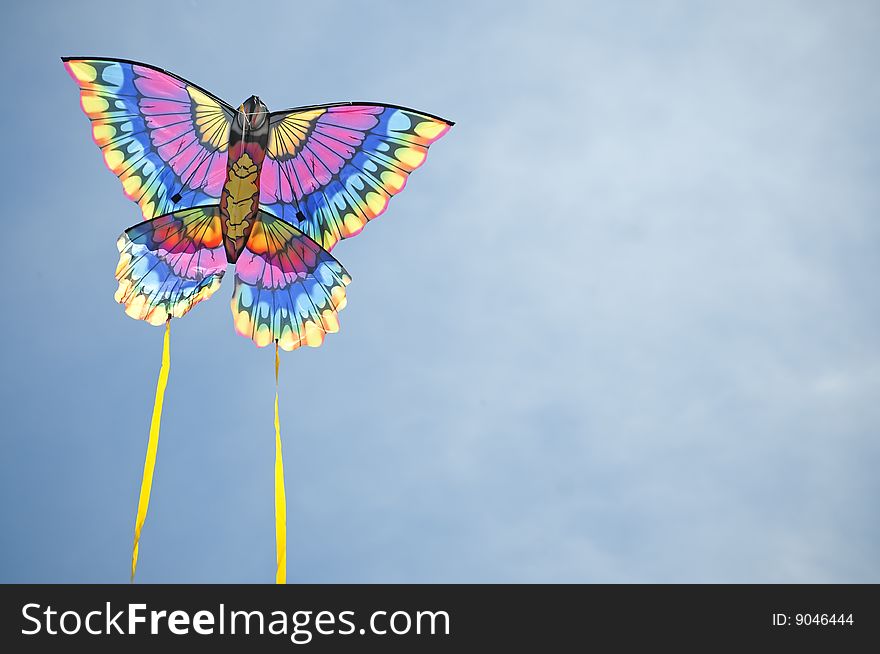 Multi-colored kite flies against a blue sky background. Multi-colored kite flies against a blue sky background