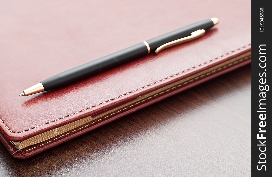 Leather notebook and a black pen on a dark desktop. Leather notebook and a black pen on a dark desktop.