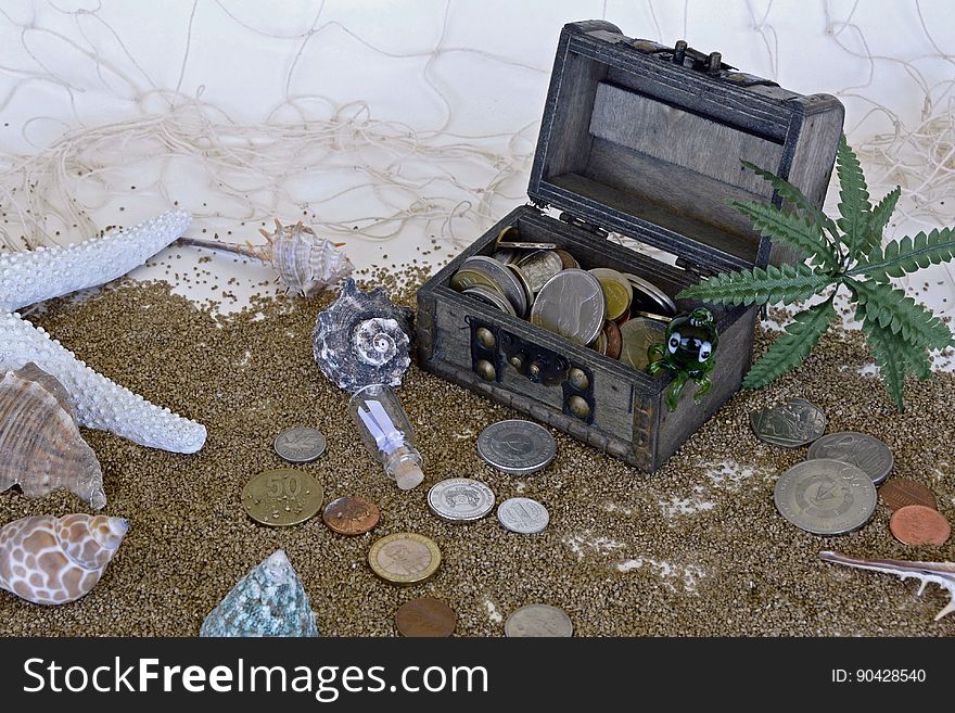 Black treasure chest on a sandy beach with coins and sea shells surrounding it , white chalk cliff background. Black treasure chest on a sandy beach with coins and sea shells surrounding it , white chalk cliff background.