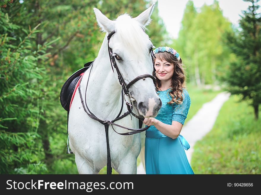 Outdoor portrait of a big gray horse and a Caucasian smiling woman in a blue dress in the forest. Outdoor portrait of a big gray horse and a Caucasian smiling woman in a blue dress in the forest.