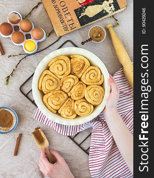 Still life on unbaked cinnamon rolls in pan with ingredients and cookbook on countertop.