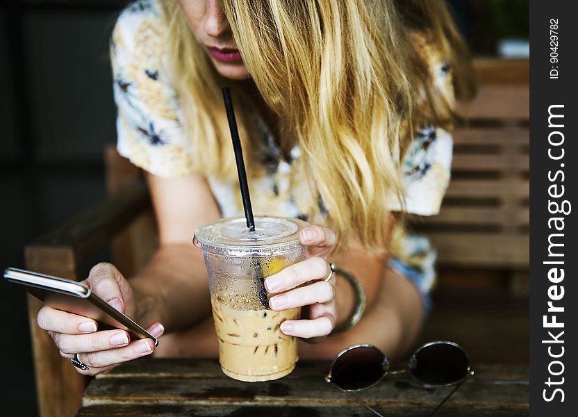 A woman reading her mobile phone while drinking an iced coffee. A woman reading her mobile phone while drinking an iced coffee.