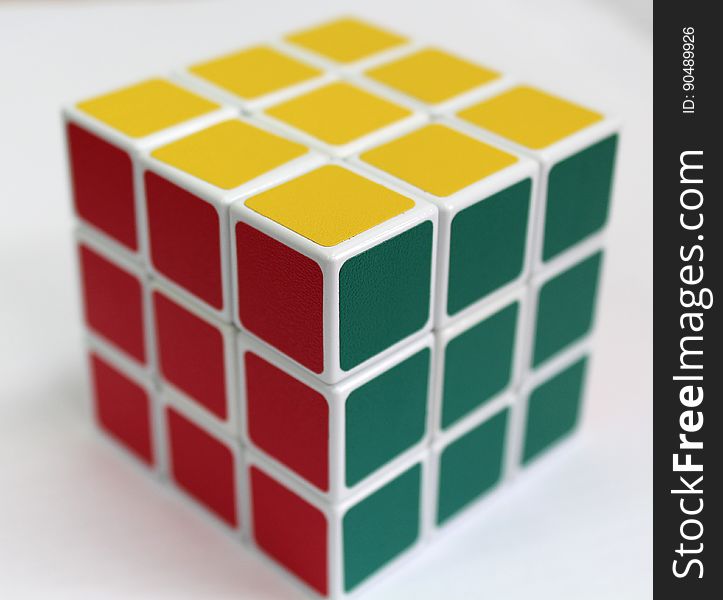 Rubik's cube with three faces showing, top has nine yellow squares, sides have nine gray and nine red squares, bright background. Rubik's cube with three faces showing, top has nine yellow squares, sides have nine gray and nine red squares, bright background.
