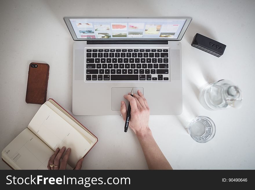 A person writing on his notebook or journal while working on a laptop seen from above. A person writing on his notebook or journal while working on a laptop seen from above.