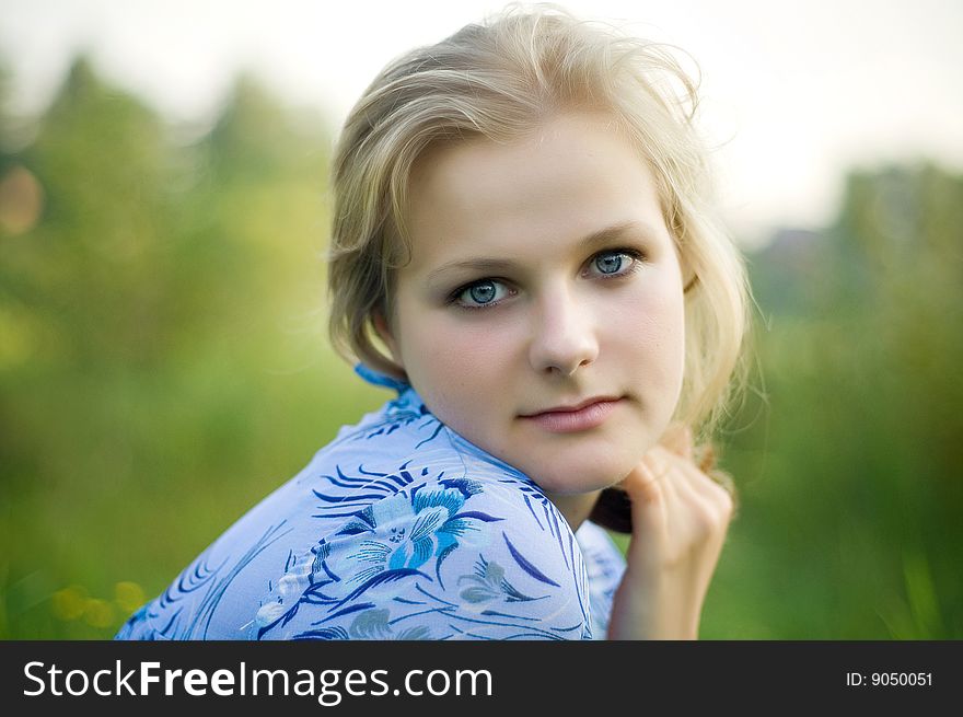 A beautiful blond haired blue eyed model sits amid tall grass