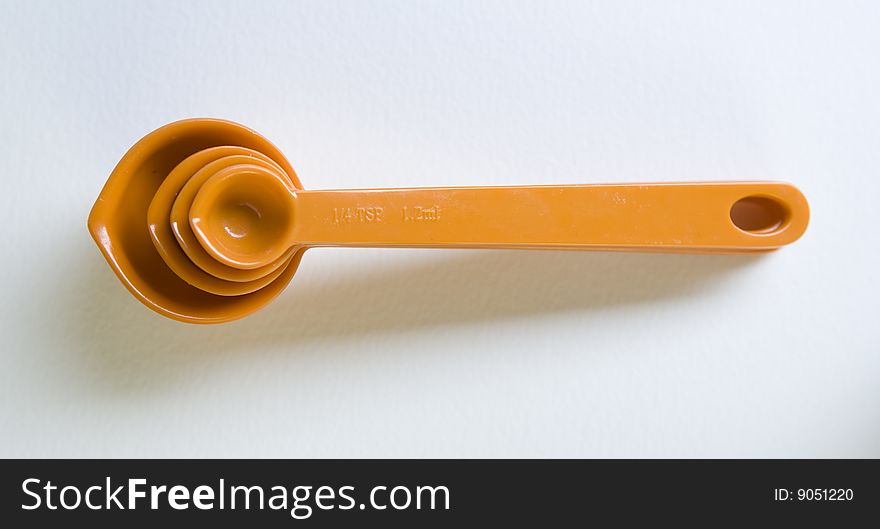 Orange measuring spoons, stacked, on white surface